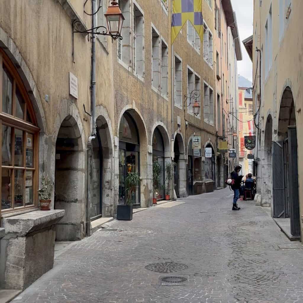 Narrow cobblestone street lined with arches and small shops in Chambéry old town. Classic scene from a family day trip French Alps.