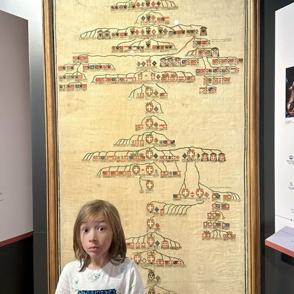 Child standing in front of a large historic family tree display inside a museum in Chambéry. Cultural stop that adds learning to a day trip from La Plagne.