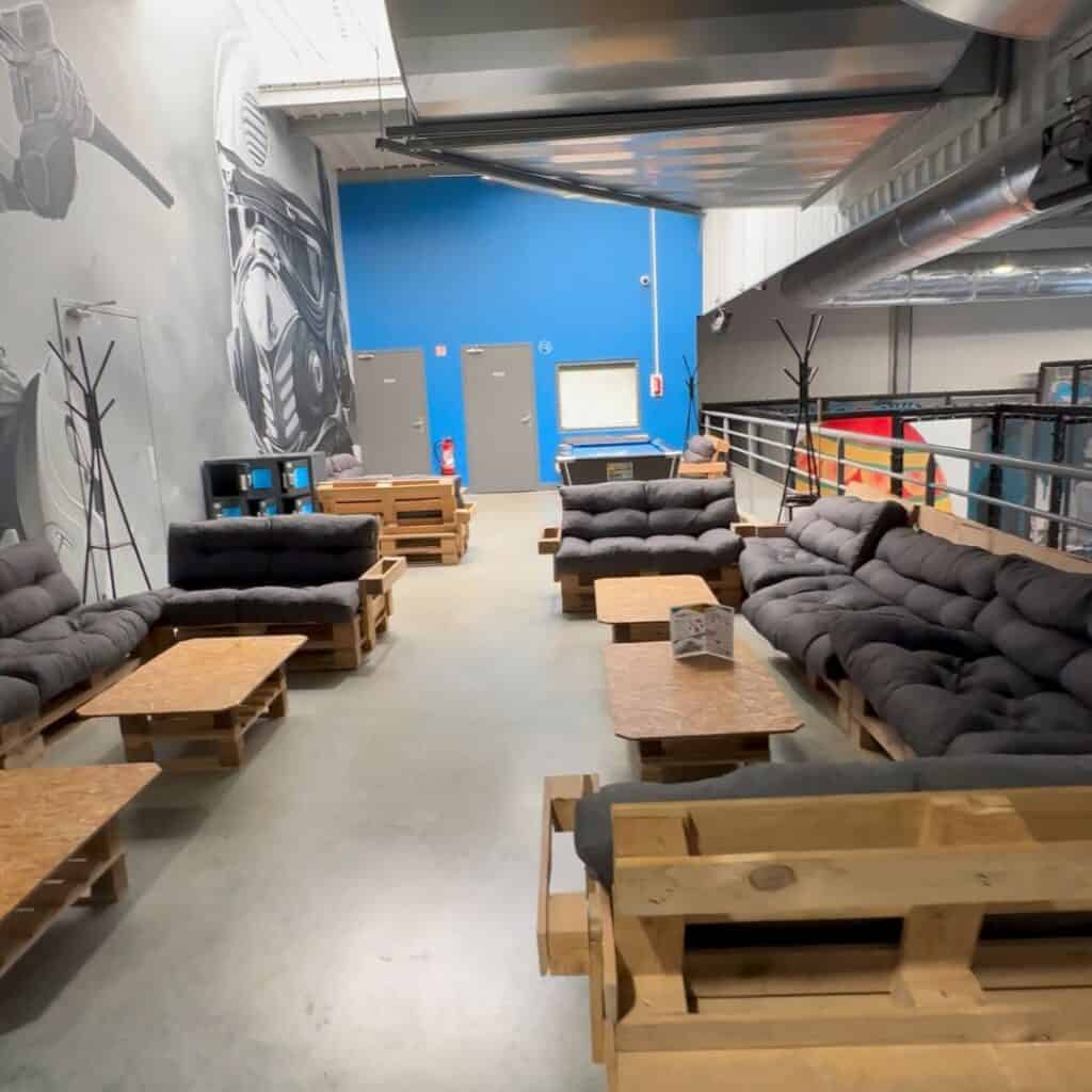 Lounge area with wooden pallet sofas and low tables in a modern indoor space. Relaxation zone for parents during a family day trip La Plagne at K Park Albertville.