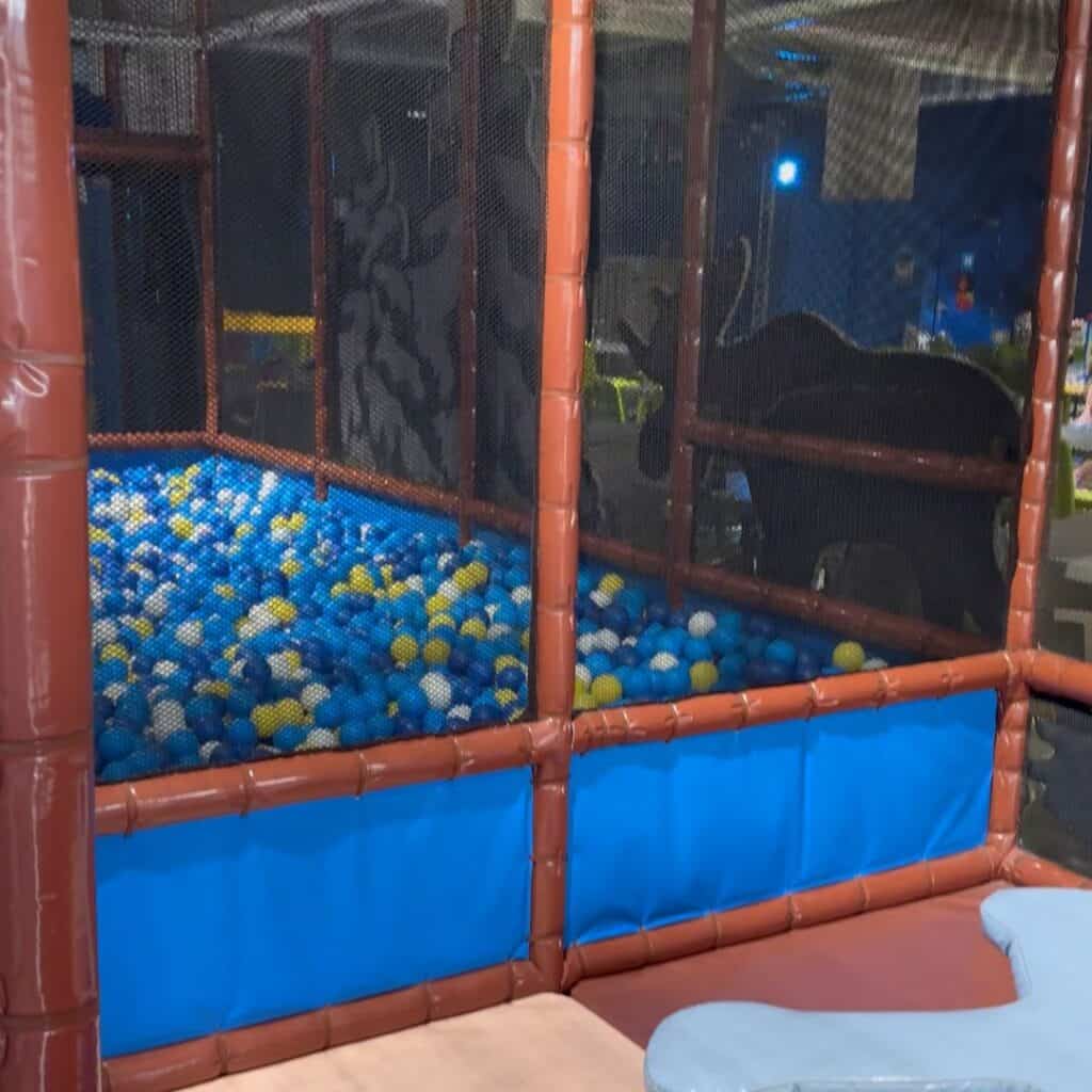 Ball pit filled with blue white and yellow balls inside a netted play structure. Play zone designed for younger kids at an indoor activities Albertville center.