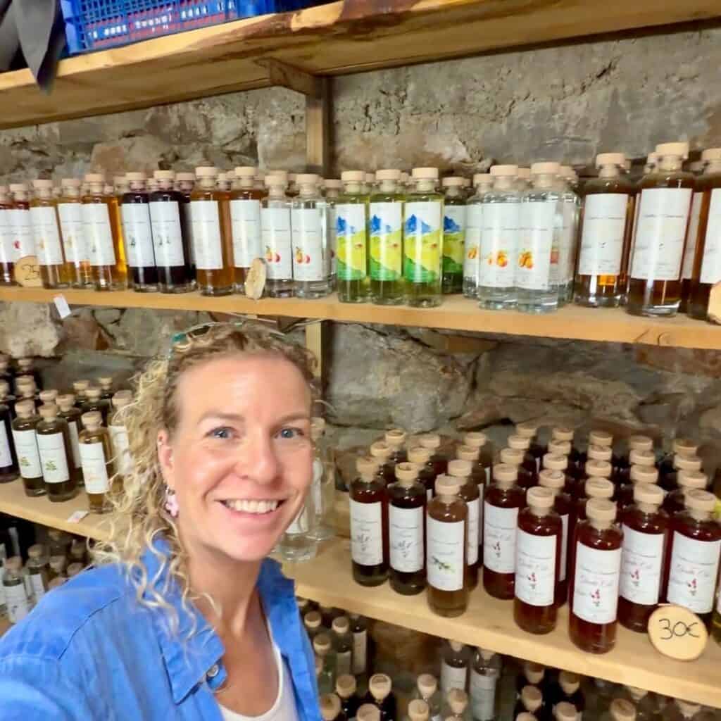 Woman standing inside Distillerie de Chantemouche surrounded by shelves of locally produced Alpine spirits and liqueurs.