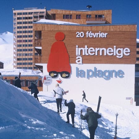 Vintage photo of skiers in front of a Plagne Centre building painted with the red Bonnet Rouge and the words "20 février Interneige à La Plagne"